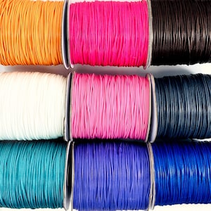 May include: Eight spools of cord in various colors, including orange, pink, white, light pink, teal, purple, dark blue, and brown. The cords are wound tightly on the spools and are ready to be used for crafting projects.