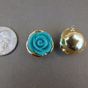 May include: Two gold-tone metal charms, one with a turquoise blue rose design and the other a smooth, round shape.