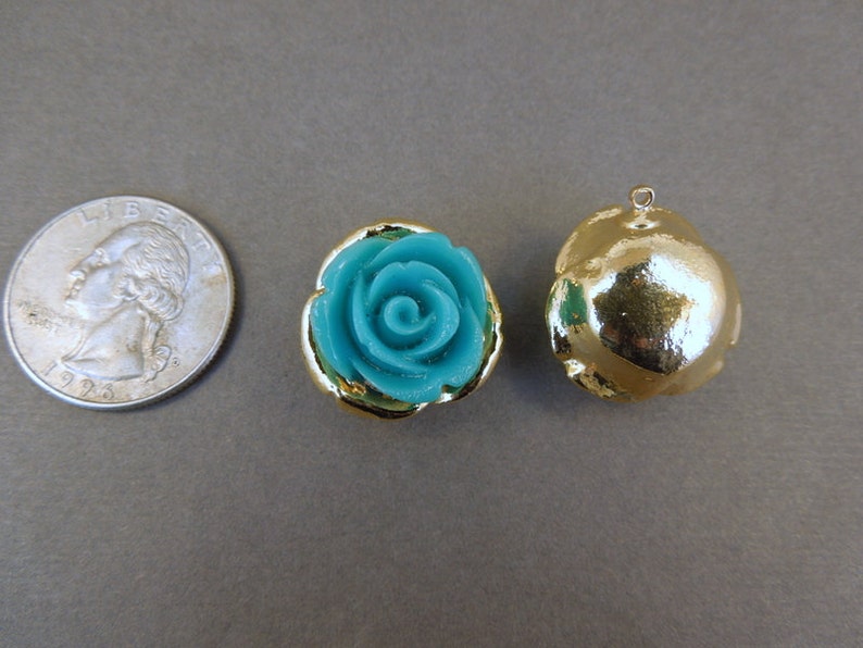 May include: Two gold-tone metal charms, one with a turquoise blue rose design and the other a smooth, round shape.
