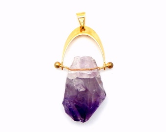 Könnte beinhalten: Ein goldener Anhänger mit einem großen, rohen Amethystkristall. Der Kristall ist tiefviolett und hat eine natürliche, unregelmäßige Form. Der Anhänger ist an einer goldenen Öse befestigt.