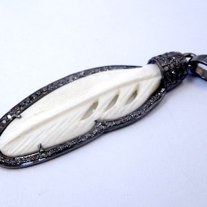 Puede incluir: Un colgante de pluma de hueso blanco con un borde de diamantes negros y una argolla de metal negro.