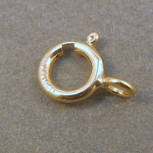 May include: Gold-toned metal clasp with a round ring and a small loop. The clasp is marked with the text "1061".
