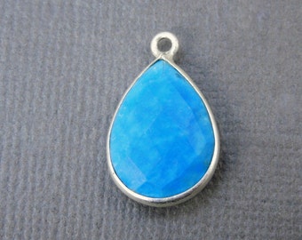 Op de afbeelding: Een traanvormige hanger met een helderblauwe edelsteen gezet in een zilveren bezel.