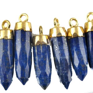 Könnte beinhalten: Ein Set mit 12 vergoldeten Lapislazuli-Edelstein-Anhängern. Jeder Anhänger hat eine facettierte, spitze Tropfenform mit einer goldenen Öse.