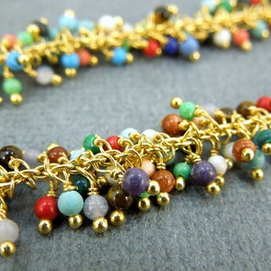 May include: A gold chain necklace with colourful gemstone beads dangling from it. The beads are in various shapes and sizes, and the chain is made of small, linked rings.