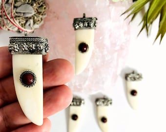 Peut inclure: Cinq pendentifs en os blanc avec des accents argentés et des incrustations de pierres précieuses rouges. Les pendentifs sont en forme de dent ou de canine.