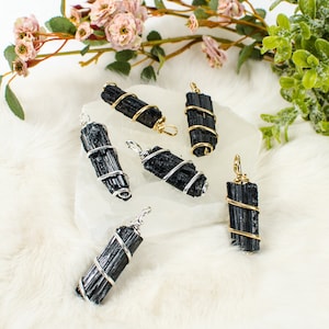 May include: Six black tourmaline pendants wrapped in silver wire. The pendants are displayed on a white surface with a white fluffy background.
