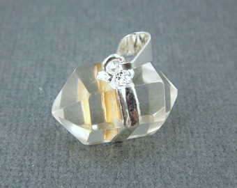 May include: A clear quartz crystal pendant with a silver bail. The crystal is faceted and has a golden hue.