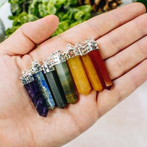 May include: Seven chakra crystal pendants in a hand. The pendants are in the colours of the chakras: purple, indigo, blue, green, yellow, orange, and red.