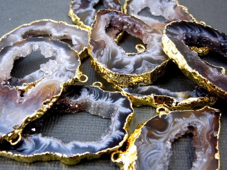 Puede incluir: Una colecci&oacute;n de rodajas de &aacute;gata con bordes chapados en oro. El &aacute;gata es una piedra natural con una variedad de colores y patrones, incluyendo blanco, marr&oacute;n y negro. Las rodajas son de diferentes tama&ntilde;os y formas, y tienen un acabado liso y pulido.