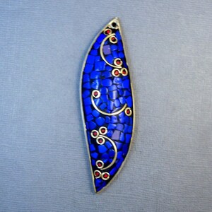Op de afbeelding: Een blauwe en gouden hanger met een moza&iuml;ekontwerp. De hanger heeft de vorm van een blad en heeft rode accenten.