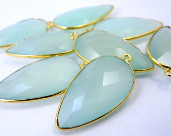 May include: A group of light blue chalcedony gemstone pendants with gold-toned metal accents. The pendants are teardrop shaped and have a faceted finish.