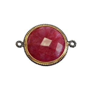 May include: A round, red gemstone pendant with a gold-toned bezel and silver-toned loops on either side.