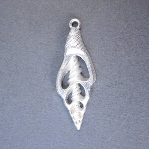 May include: Silver pendant shaped like a seashell with a detailed, intricate design. The shell is open and reveals a spiral inside.