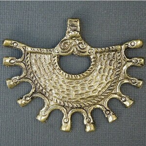 May include: A gold-toned metal pendant with a decorative design. The pendant has a large, open circle in the center and a series of smaller circles around the edge. The pendant is intricately detailed and has a textured surface.