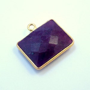 May include: A gold-plated pendant featuring a rectangular, faceted purple gemstone.