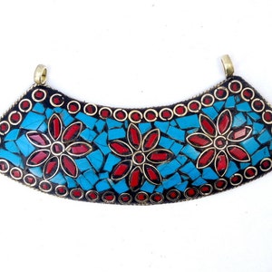 May include: A curved pendant made of brass with a mosaic design. The mosaic is made of turquoise and red stones and features three stylized flowers.