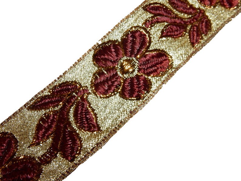 May include: Gold trim with burgundy floral embroidery. This trim features a repeating pattern of flowers and leaves.