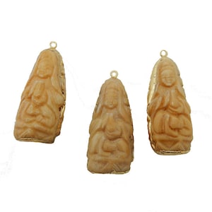 May include: Three gold-trimmed pendants featuring detailed carvings of a seated figure. The pendants are made of a light brown material, possibly bone or ivory.