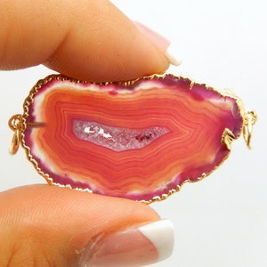 May include: A pink and orange agate slice pendant with a gold-toned edge. The pendant has a natural, organic shape and is perfect for jewellery making.