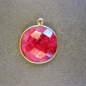 May include: A round, red gemstone pendant with a gold setting. The gemstone is faceted and has a shiny finish.