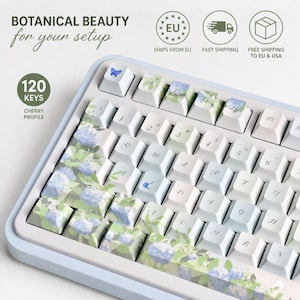 Könnte beinhalten: Eine hellblaue und weiße Tastatur mit floralen Tastenkappen. Die Tastenkappen zeigen ein Hortensien-Design mit grünen Blättern und blauen Blüten. Die Tastatur hat 120 Tasten und ein Cherry-Profil. Der Text "BOTANICAL BEAUTY for your setup" ist sichtbar.