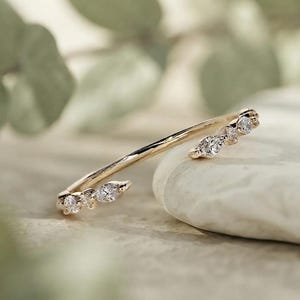 Peut inclure: Une bague ouverte en or dotée de deux extrémités ornées de petites pierres transparentes, taillées en marquise et en rond. L'anneau est fin et poli, avec les pierres disposées en grappe à chaque extrémité du design ouvert.