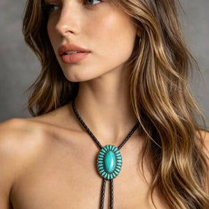 May include: Oval turquoise bolo tie with a black leather cord. The turquoise stone is surrounded by a silver-coloured metal frame. The bolo tie has a decorative silver-coloured metal tip.