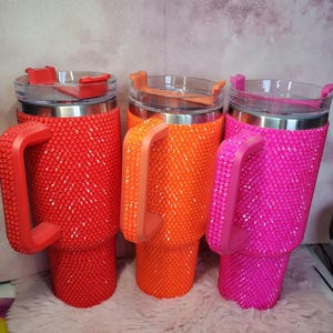 Pu&ograve; includere: Tre bicchieri tempestati di strass rossi, arancioni e rosa. Ogni bicchiere ha un manico e un coperchio abbinati con un'apertura trasparente a ribalta. I bicchieri sono ricoperti di piccoli abbellimenti scintillanti.