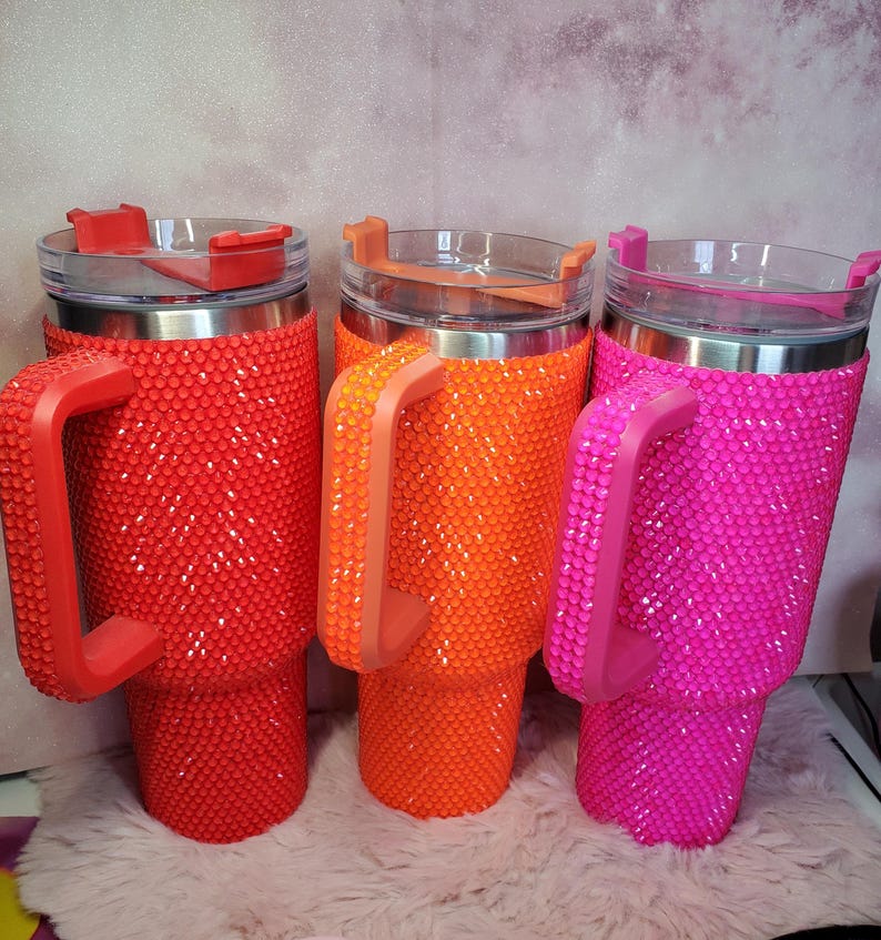 Pu&ograve; includere: Tre bicchieri tempestati di strass rossi, arancioni e rosa. Ogni bicchiere ha un manico e un coperchio abbinati con un'apertura trasparente a ribalta. I bicchieri sono ricoperti di piccoli abbellimenti scintillanti.