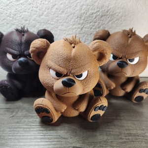 Könnte beinhalten: Drei braune Bärenfiguren mit wütenden Ausdrücken. Die Bären haben detaillierte Merkmale, darunter gerunzelte Augenbrauen, kleine Ohren und schwarze Nasen. Die Figuren sitzen auf einer Holzoberfläche.