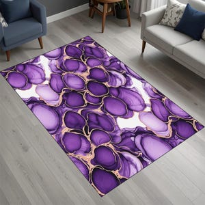 Könnte beinhalten: Ein rechteckiger Teppich mit einem abstrakten Design in Lila- und Weißtönen, mit goldfarbenen Umrissen. Das Muster des Teppichs ähnelt organischen Formen und schafft eine moderne und künstlerische Ästhetik. Der Teppich liegt auf einem hellgrauen Holzboden.