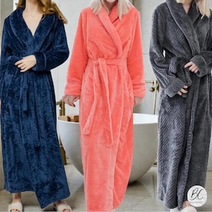 May include: Three plush bathrobes in navy blue, coral, and gray. Each robe has a shawl collar, long sleeves, and a matching belt. The robes are floor-length and made of a soft, textured fabric, perfect for lounging.