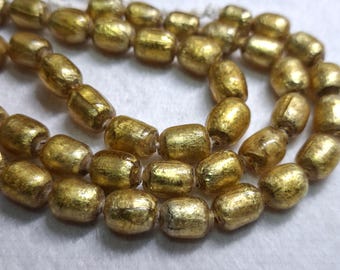 May include: Close-up of a strand of golden-colored beads. The beads are barrel-shaped and have a textured, metallic finish. The beads are strung together on a white string, creating a necklace or bracelet.