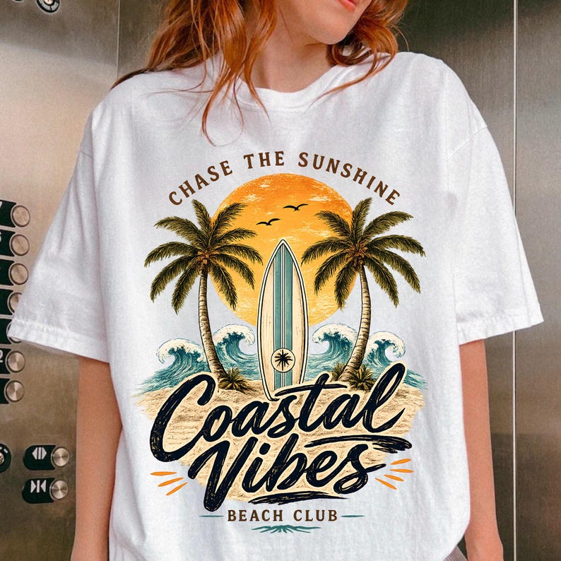 May include: White t-shirt with a beach-themed graphic. The design features a sunset, palm trees, a surfboard, and ocean waves. Text includes "CHASE THE SUNSHINE" and "Coastal Vibes Beach Club".