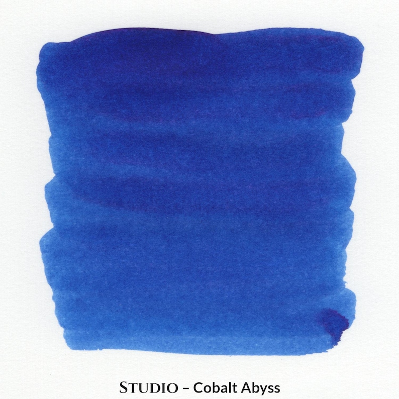 Puede incluir: Una muestra de tinta azul profundo, etiquetada como "STUDIO - Cobalt Abyss", sobre un fondo blanco. La tinta se aplica en forma rectangular, con pinceladas visibles y variaciones de color, mostrando su profundidad y textura.