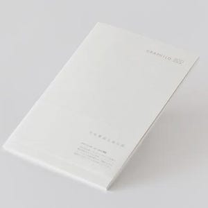 May include: A white notebook with the text "GRAPHILO 000" printed in gray on the top right corner. The notebook is slightly angled, showing its cover and a portion of its pages. The background is a plain white.