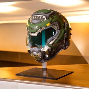以下が含まれることがあります： スタンドに展示された、詳細な緑と銀色のヘルメット。ヘルメットは、ティール色のバイザーを備えています。デザインは、SFまたはゲームのテーマを示唆しています。レプリカまたはコレクターズアイテムである可能性があります。