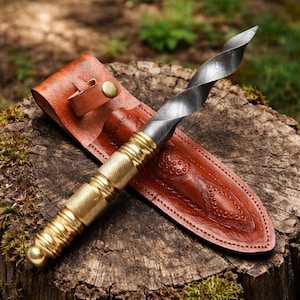 May include: A handcrafted knife with a twisted blade and a brass handle, resting in a brown leather sheath. The blade has a unique pattern, and the sheath features decorative stitching and a snap closure. The knife is displayed on a wooden surface.