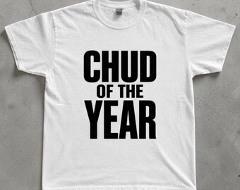 May include: A white short-sleeved t-shirt featuring the bold black text CHUD OF THE YEAR printed in a sans-serif font across the centre of the chest. The garment has a classic crew neckline and a standard fit with short sleeves and a straight hem.