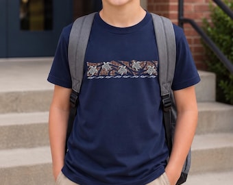 May include: A navy blue short-sleeve t-shirt featuring a horizontal band across the chest. The band displays a brown patterned background with four white sea turtle illustrations and a row of white wave motifs along the bottom edge.