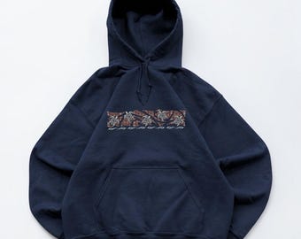 May include: A navy blue hooded sweatshirt featuring a horizontal band across the chest. The band displays a brown and white patterned design with a series of small sea turtle illustrations and wave motifs centered on the front of the garment.