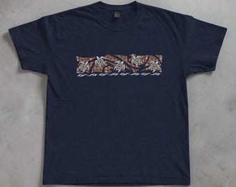 May include: A navy blue short-sleeved t-shirt featuring a central rectangular graphic. The design displays five white sea turtles swimming across a brown patterned background with geometric shapes, finished with a white wave line at the bottom.
