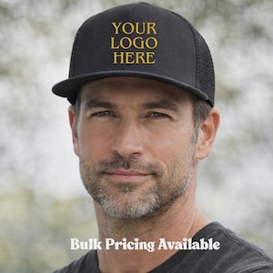 May include: Black trucker hat with a flat brim and mesh back. The hat features the text "YOUR LOGO HERE" in gold lettering on the front. The phrase "Bulk Pricing Available" is displayed below.
