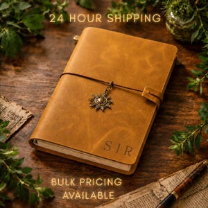 May include: A tan leather journal with a sun charm and the word "SIR" embossed on the cover. The journal is closed with a brown leather strap. The image also includes the text "24 HOUR SHIPPING" and "BULK PRICING AVAILABLE".