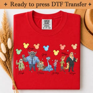 Puede incluir: Una camiseta de color rojo brillante con un estampado gr&aacute;fico de varios personajes animados de Zootopia, incluidos Flash, Bogo, Nibbles, Judy Hopps, Nick Wilde y el alcalde Lionheart, cada uno con un globo de colores, con el texto Ready to press DTF Transfer.