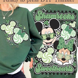 Pode incluir: Uma camisola verde-escura com uma transferência DTF com o texto Ready to press DTF Transfer. O gráfico inclui duas personagens de rato de desenhos animados com óculos em forma de coração, rodeadas por espirais verde-claras e trevos.