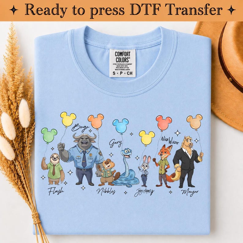 Puede incluir: Una camiseta azul claro con un estampado gr&aacute;fico de varios personajes animados, cada uno sosteniendo un globo de color con forma de cabeza de rat&oacute;n. Los personajes est&aacute;n etiquetados con nombres como Flash, Bogo, Gary, Nibbles, Judy Hopps, Nick Wilde y Mayor.