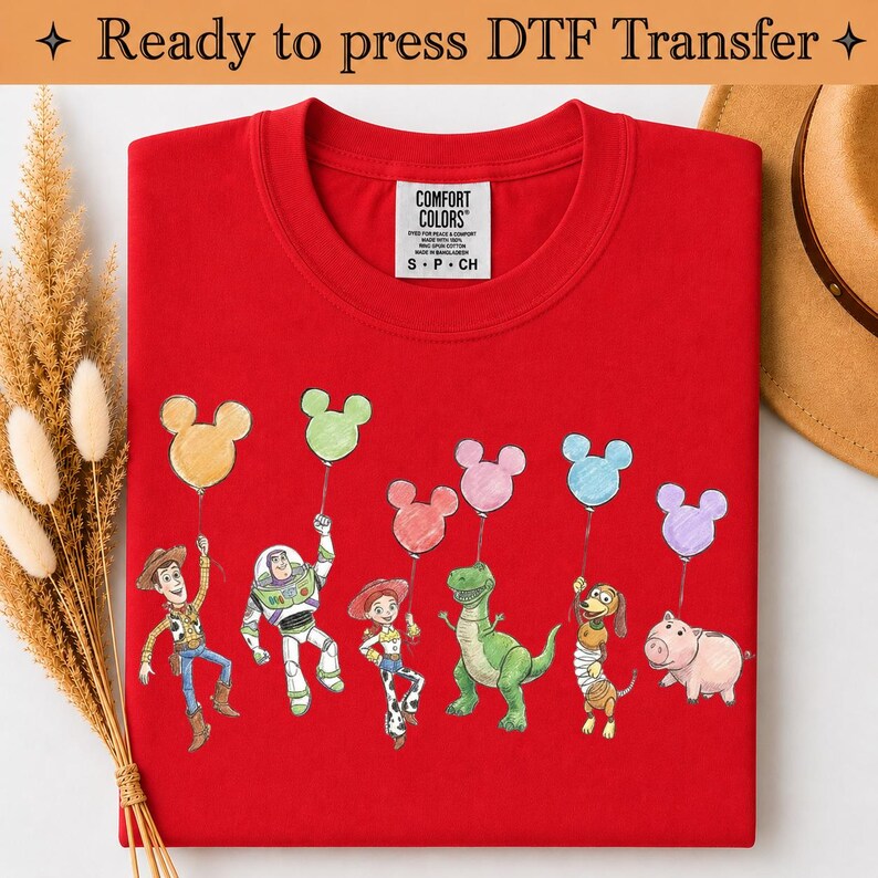 Puede incluir: Una camiseta roja con un gr&aacute;fico de seis personajes de dibujos animados de Toy Story, cada uno sosteniendo un globo con forma de Mickey Mouse de diferentes colores. La camiseta tiene una etiqueta Comfort Colors en el cuello y el texto Ready to press DTF Transfer.