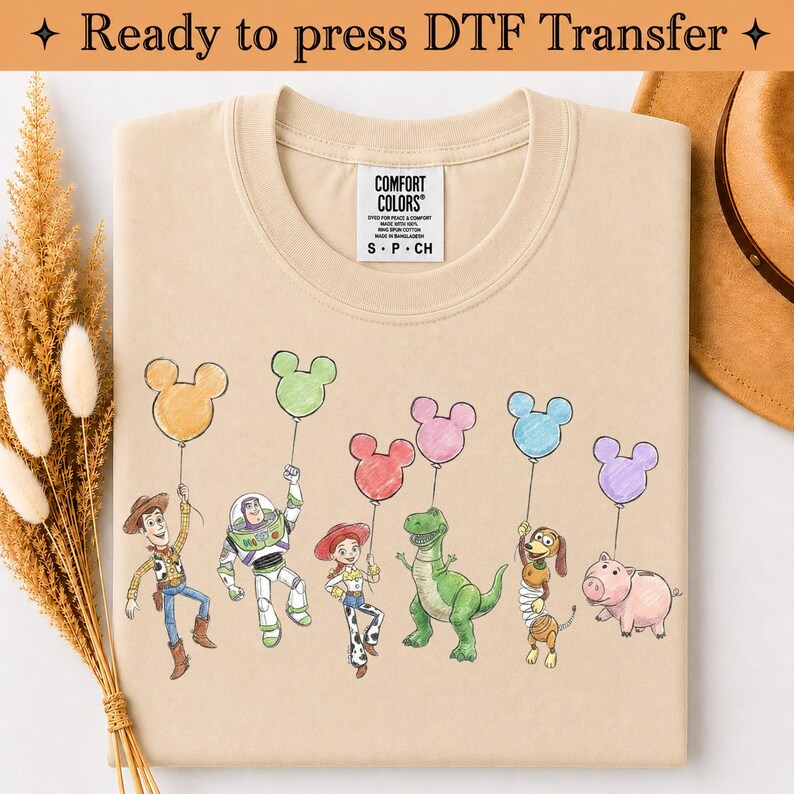 Puede incluir: Una camiseta beige con un estampado gr&aacute;fico de seis personajes animados sosteniendo globos de colores con forma de Mickey Mouse. Los personajes incluyen un vaquero, un guardi&aacute;n espacial, una vaquera, un dinosaurio verde, un perro y un cerdo.